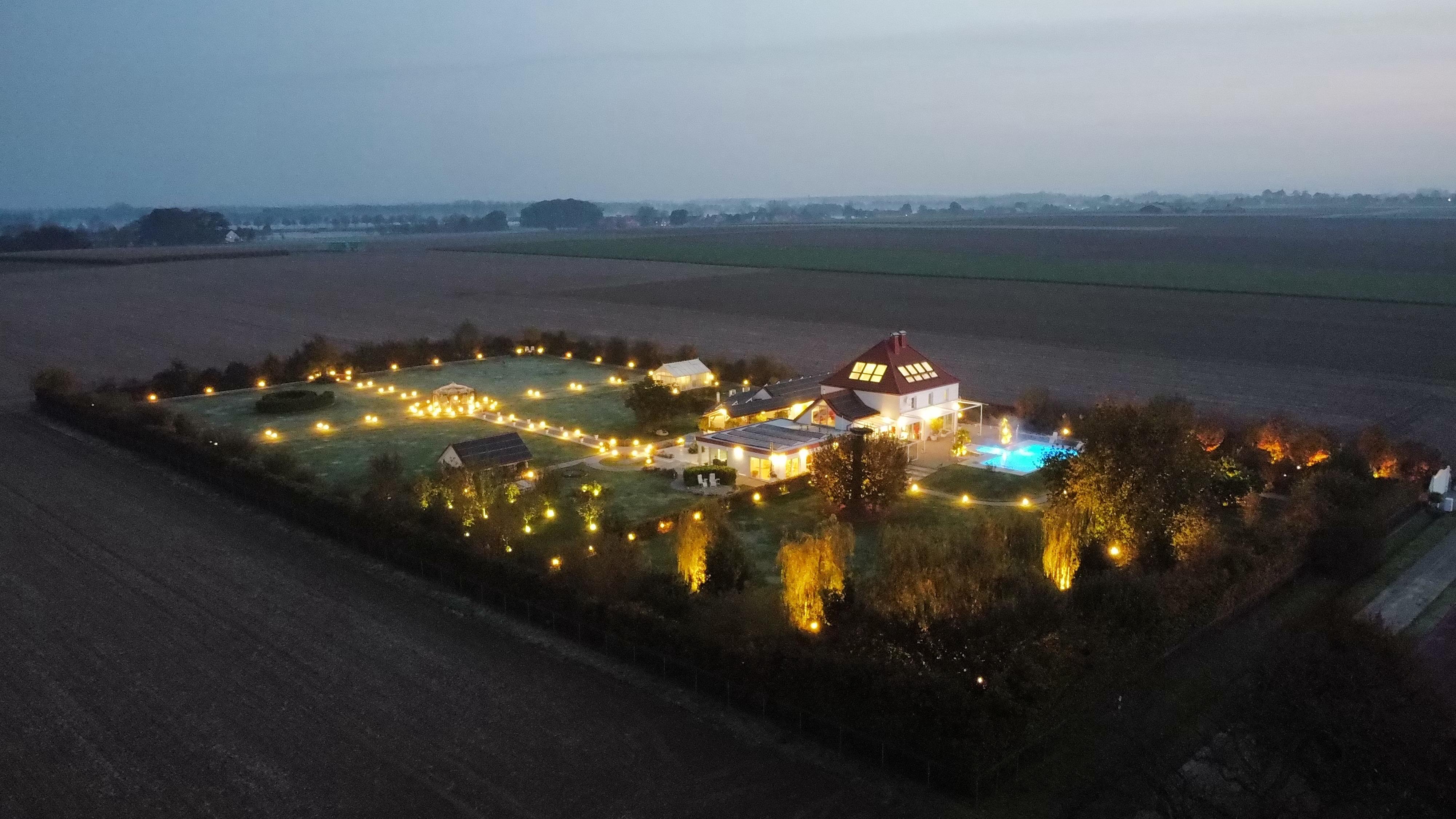 Luftaufnahme des beleuchteten Anwesens bei Nacht mit Garten, Pool und umliegendem Gelände